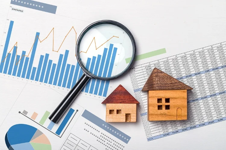 Magnifying glass on real estate documents spread across a table with some house figures 