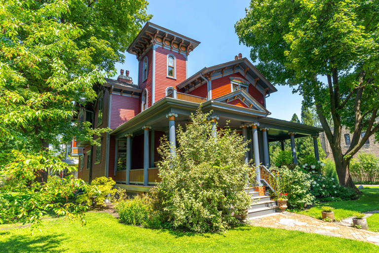 Picture boasts a charming house embraced by abundant foliage, adorned with vibrant hues that exude cheerfulness.