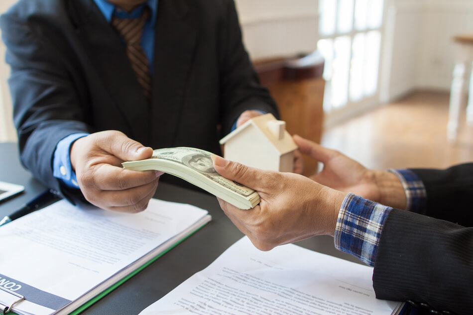 picture displays two hands someone is handing a cash and other one taking a house figure ( house sale) 