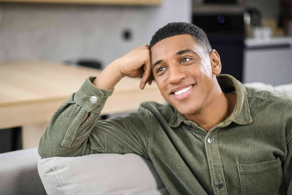 smiling man setting on his couch, leaning on his hand. and daydreaming.