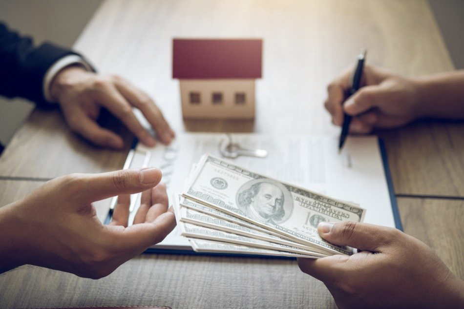 picture displays a hand of a person selling his greenville house to other man and handing him some cash while signing the contract